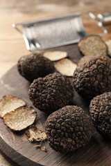 Whole and cut black truffles with wooden board on table