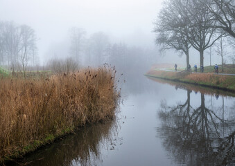 valleikanaal or valley canal and men on bicycle near scherpenzeel in the netherlands on misty winter day