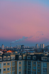 view of the city at dawn. blue smoke comes out of the chimney. pink sky 