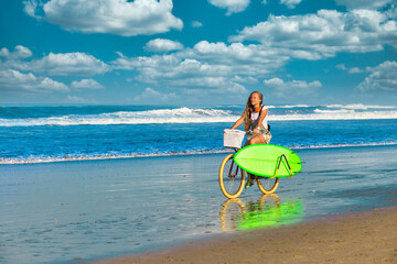 Naklejka na ściany i meble Young woman with surfboard and bicycle on the beach.