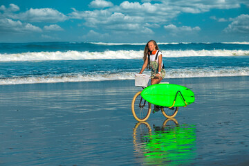 Young woman with surfboard and bicycle on the beach.