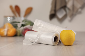Rolls of plastic bags and fresh apple on white table