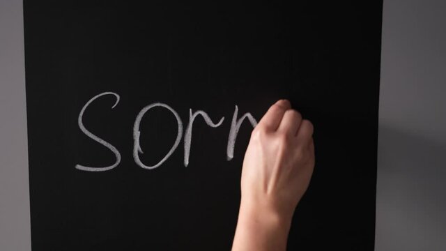girl writes on a chalk board with chalk the word sorry
