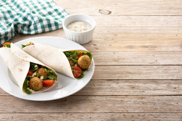 Tortilla wrap with falafel and vegetables on wooden table. Copy space