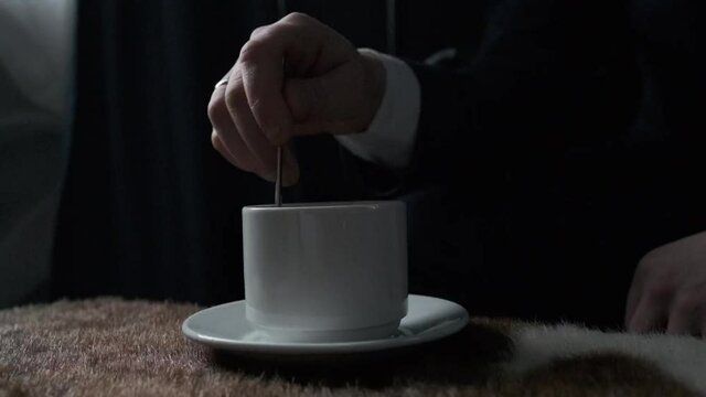 man stirring a cup of coffee standing on the table