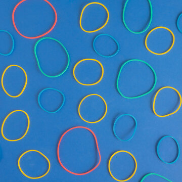 Creative pattern of hair ties rubber bands on a vibrant blue background. Square frame. Yellow, red, blue, green color. Flat lay arrangement.