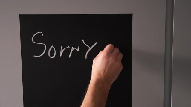 boy writes on a chalk board with chalk the phrase sorry I am gay