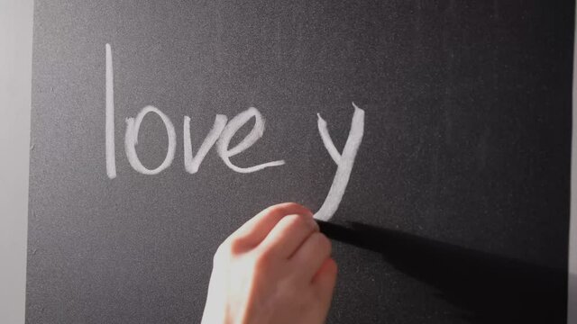 girl writes on a chalk board with chalk the phrase love you