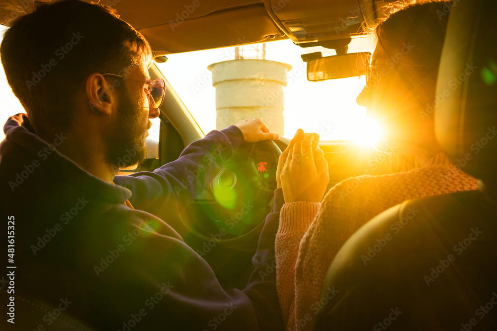 Wall mural Young romantic couple sitting in car holding hands. Drive on warm sunny day. Concept of youth, love and lifestyle. Authentic real people. View from rear seat. Road trip. Soft focus