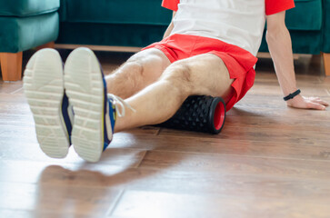 A young man in red shorts is doing exercises on a foam roller, works out of the muscles with a massage roller. Athletic man using a foam roller to relieve sore muscles after a workout