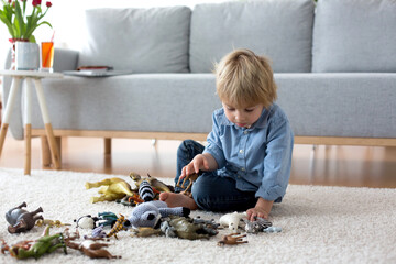 Cute blond child, toddler boy, playing at home with dinosaurs