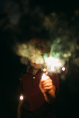 Happy boy holding burning fireworks at the night outdoors