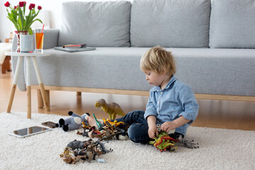 Cute blond child, toddler boy, playing at home with dinosaurs