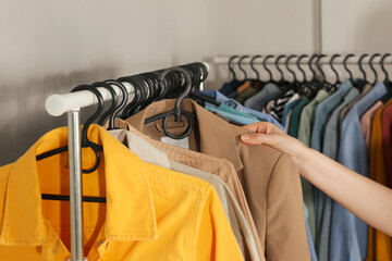 Woman picking clothes from rack indoors, closeup. Fast fashion