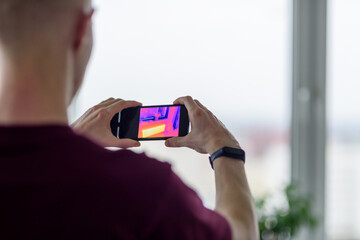 Person doing thermal scanning or imaging of apartment with smartphone app. Thermographic Inspection to check effectiveness of insulation