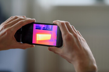 Person doing thermal scanning or imaging of apartment with smartphone app. Thermographic Inspection to check effectiveness of insulation