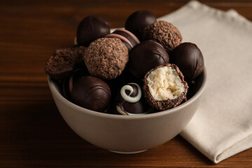 Many different delicious chocolate truffles in bowl on wooden table