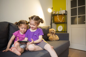 sister's children are sitting at home on couch, looking at phone, communicating via video. kids gadget apps