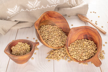 Dry organic green lentils in three wooden cups on a wooden table.