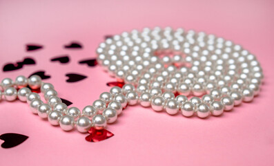 A pearl necklace lies on a pink background