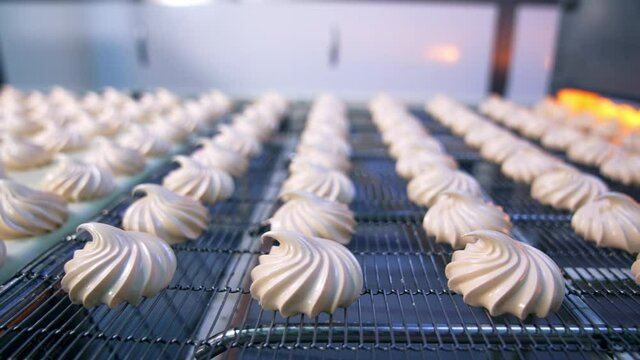 Tasty zephyr candies moving on the conveyor grid. Close up. Automated production of sweets at factory. Blurred background.