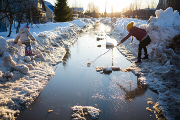 children play in puddle on street in early spring. snow melting on road. weather thaw. fun game...