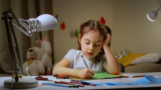Funny cute little artist girl playing alone, drawing coloring with pencils. Smart preschooler enjoying creative art while sitting at a table in the bedroom. the concept of children's development.