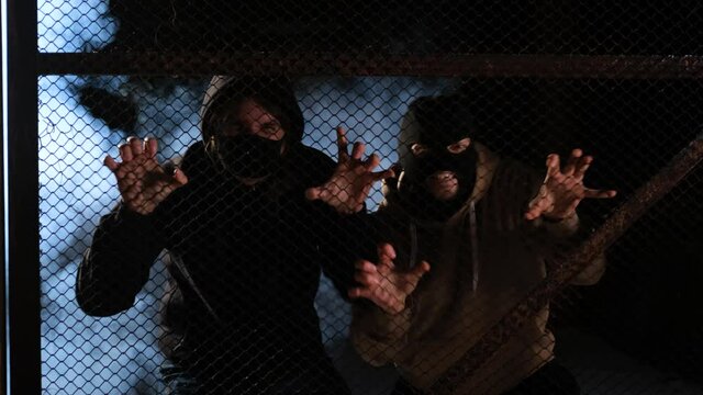 Two masked men are trying to break down the fences. Smoke in the background. The concept of pogroms and aggressive protests, uprisings and overthrow of power