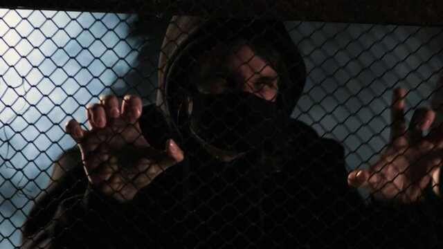 An aggressive masked activist tries to break down a fence amid smoke. The concept of protests, uprisings, robberies and clashes with the police