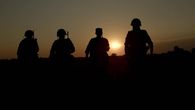 Group of four soldiers in combat helmets and ammunition walking across field.