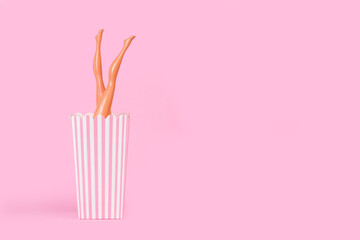 Piernas de muñeca levantadas para arriba dentro de una caja de cartón sobre un fondo rosa pastel. Vista de frente. Copy space