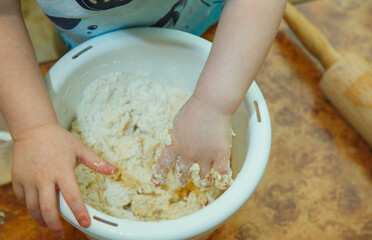 child kneading the dough with his hands in a white bowl