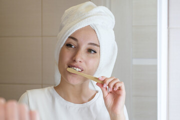 An attractive young woman brushes her teeth in the bathroom in the morning. A beautiful girl looks in the mirror while using an eco-friendly toothbrush with whitening toothpaste