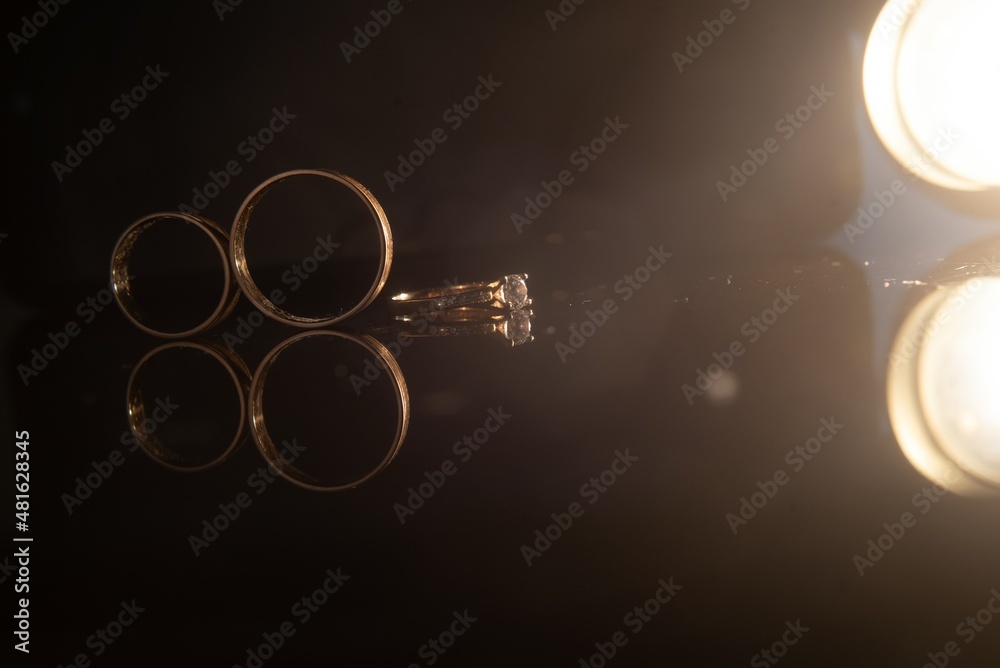 Wall mural Elegant wedding rings for the bride and groom on a black background with highlights, macro, selective focus