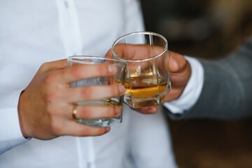 Male hands holds glasses with whiskey on black background. Cheers, close up