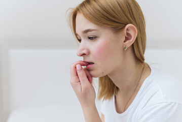 A young woman sits in bed, worries and bites her nails. Worried casual woman sitting on her bed in bedroom