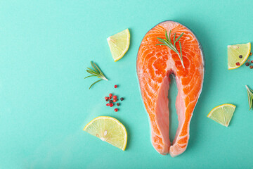Uncooked raw fresh fish salmon steak top view on blue background with rosemary, lemon wedges and spices, delicacy healthy fish cooking and nutrition concept flat lay copy space