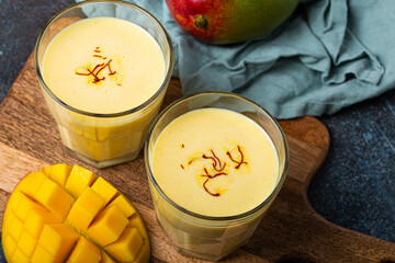 Healthy Indian Ayurveda drink mango lassi in two glasses on rustic concrete table with fresh ripe...