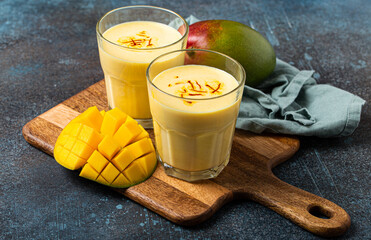 Healthy Indian Ayurveda drink mango lassi in two glasses on rustic concrete table with fresh ripe...
