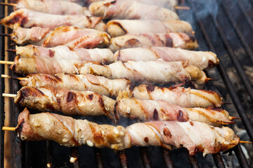 Meat wrapped in bacon on wooden skewers is fried with smoke on a grill.