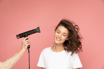 Portrait of curly woman with hairdryer and long cord on pink background