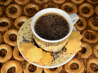 A cup of coffee with cookies on the background of small bagels.