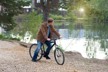 Obraz premium An adult man in a corduroy brown jacket rides a bicycle in a park along the river.