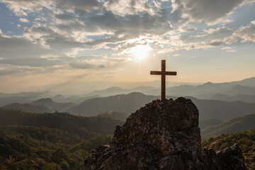 Silhouettes of crucifix symbol on top mountain with bright sunbeam on the colorful sky background - obrazy, fototapety, plakaty