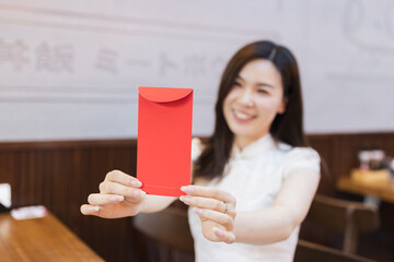 Beautiful young asian woman in traditional white dress named cheongsam sitting in Japanese restaurant or cafeteria and waiting ordered food. Girl holding red envelope. Restaurant interior decorated