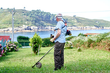 Senior man in protective shield mask mowing grass with mower