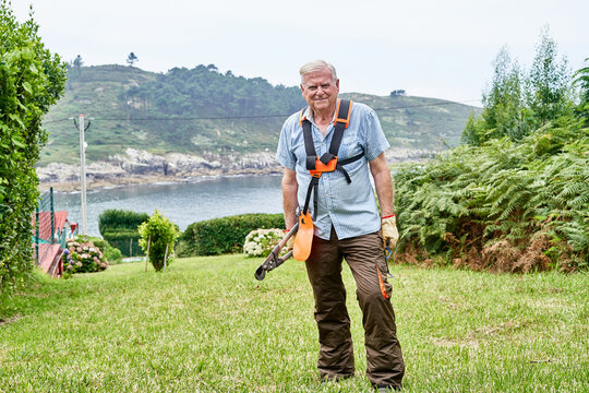 Smiling senior man gardener with garden instrument in grassy lawn