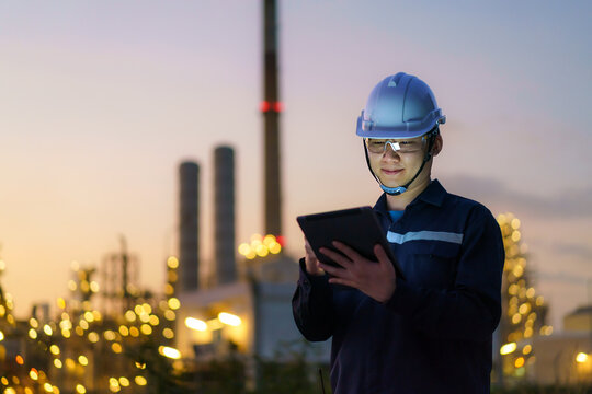 Asian Man Petrochemical Engineer Working At Night With Digital Tablet Inside Oil And Gas Refinery Plant Industry Factory At Night For Inspector Safety Quality Control..