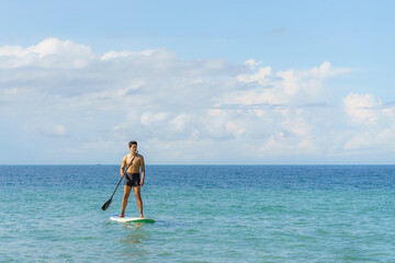 Obraz premium Asian man exercising sup board in turquoise tropical clear waters in summer day..