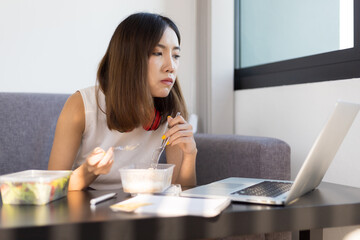 Woman eating lunch while working on laptop at home during the day. Work from home and social...